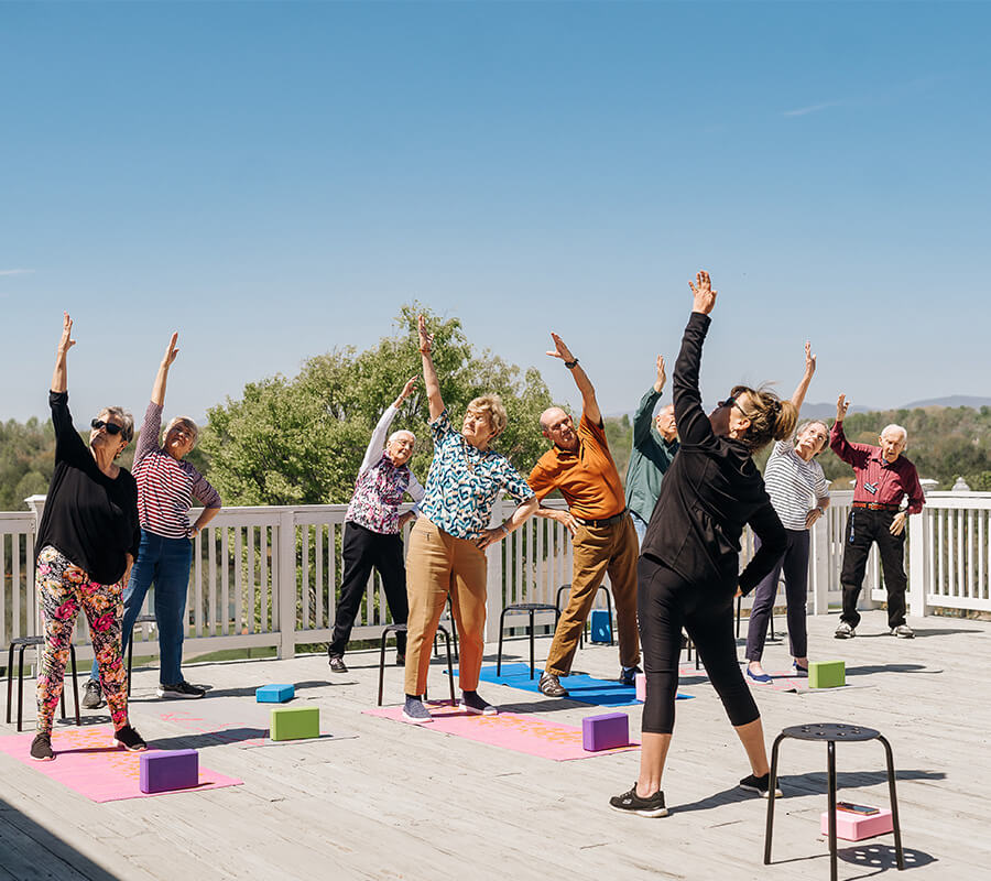 Group of seniors practicing yoga outdoors on a sunny deck with an instructor.
