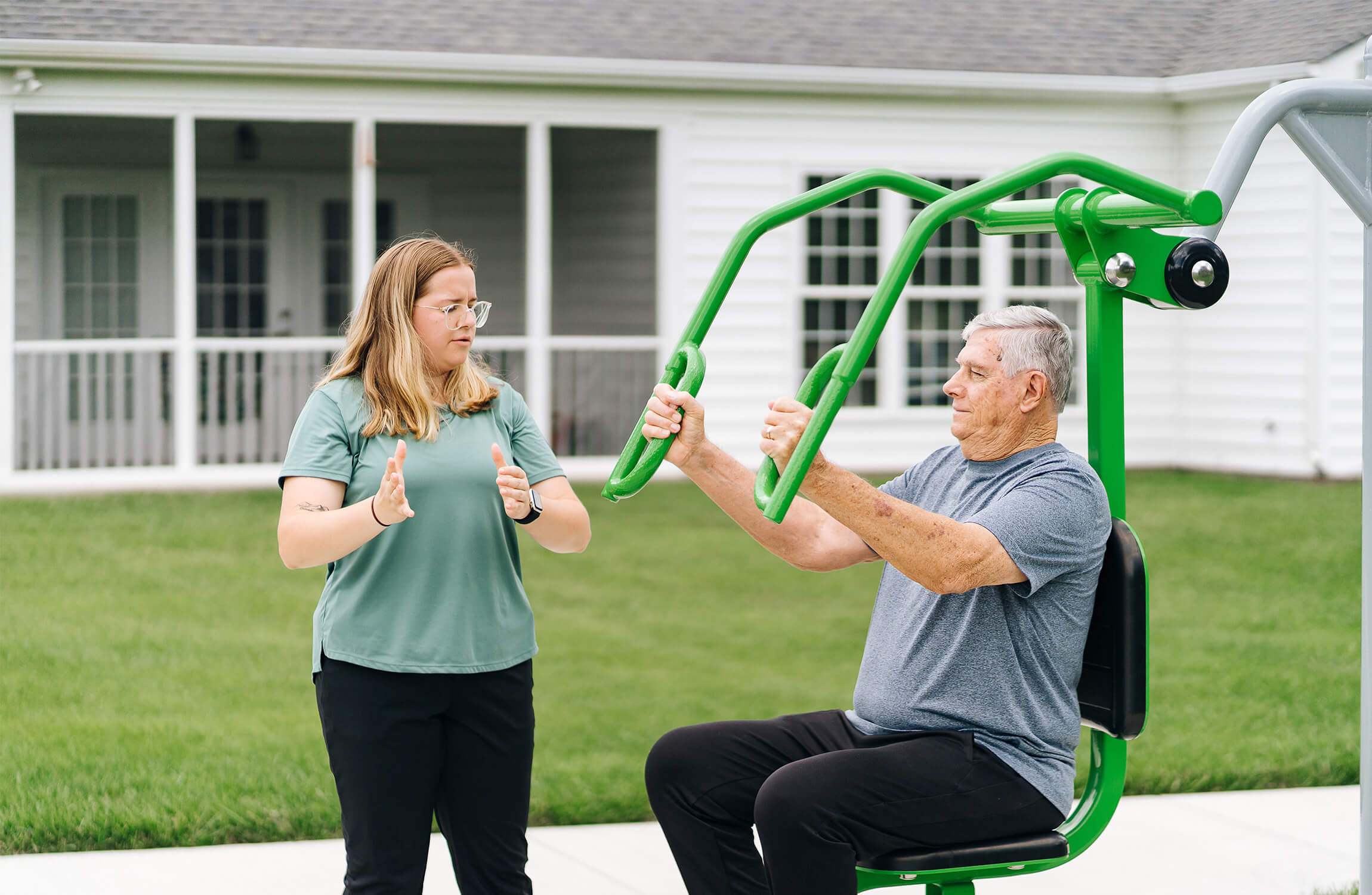 Guided Outdoor Exercise for Seniors Senior man exercising on outdoor machine with guidance from an instructor.