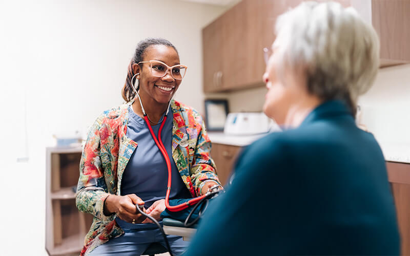 Healthcare worker smiling while taking blood pressure of a senior woman.