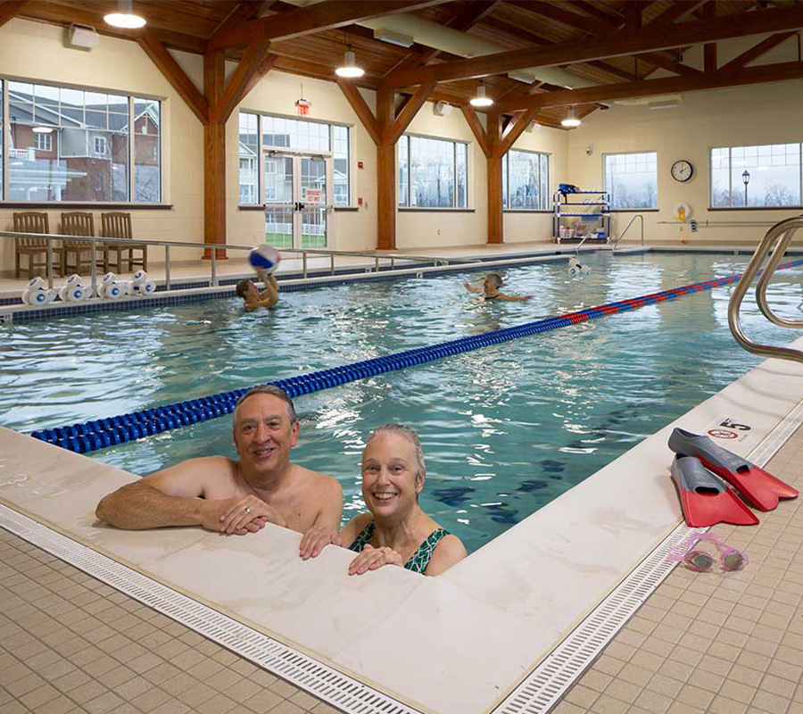 Residents enjoy swimming in indoor pool with large windows in community center.