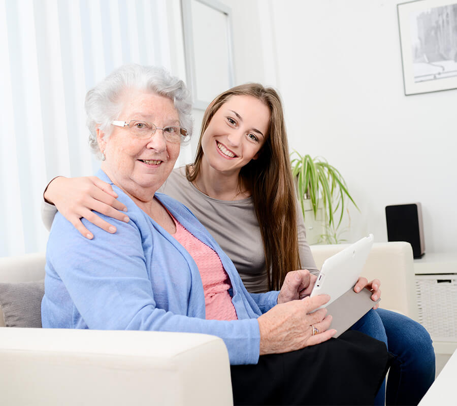 Smiling woman with elderly lady holding a tablet indoors.