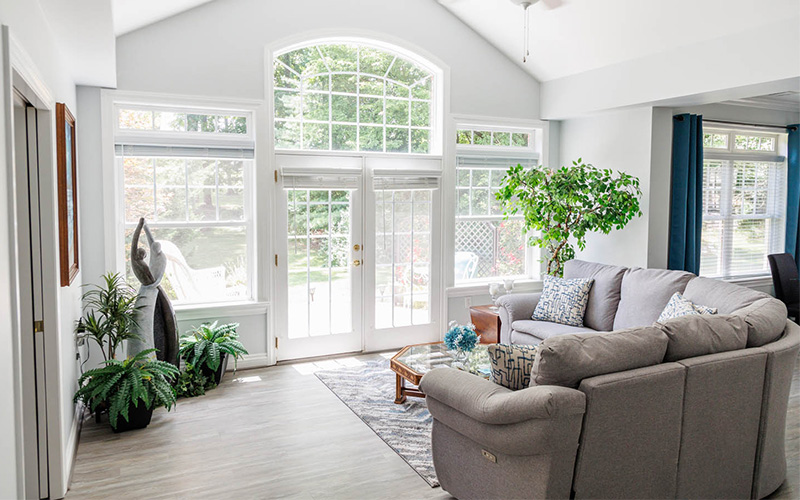 Inviting Living Room in Community Unit Bright living room with large windows, gray sofa, plants, and coffee table.