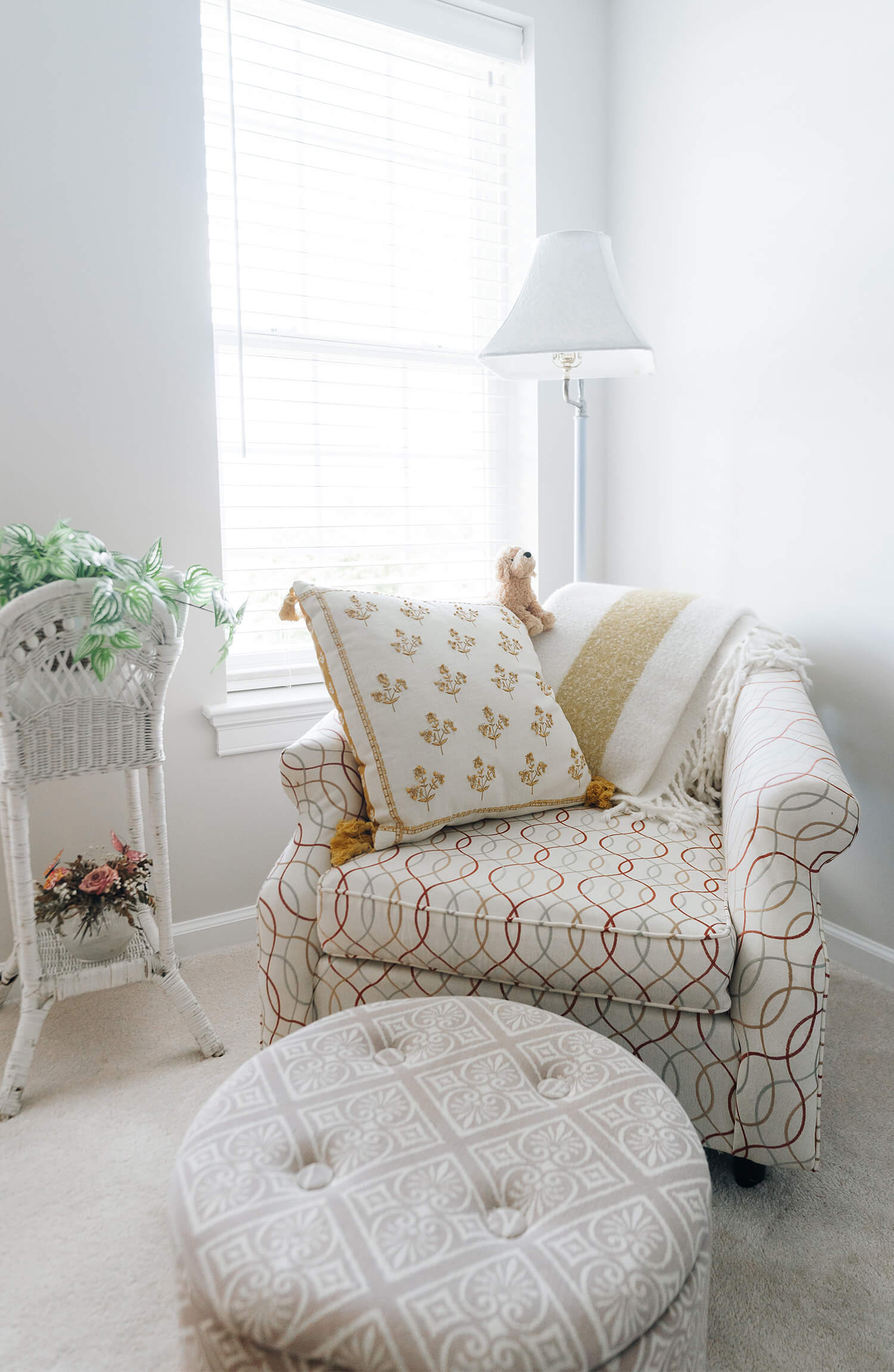 Cozy living space with patterned chair, pillow and ottoman by a bright window.