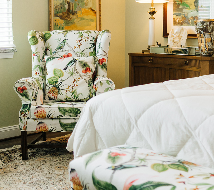 Floral armchair and white quilted bed in cozy room setup.