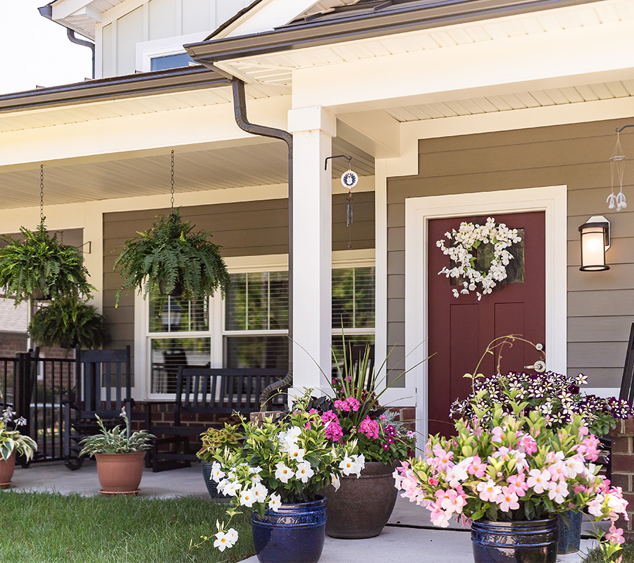 Charming porch with flowers and rocking chairs in front of a units door.