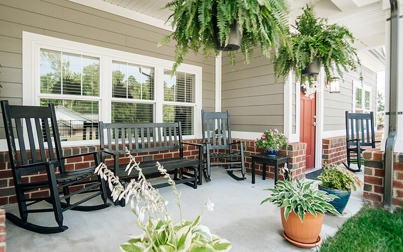 Welcoming porch with black rocking chairs and potted plants in a senior living community.