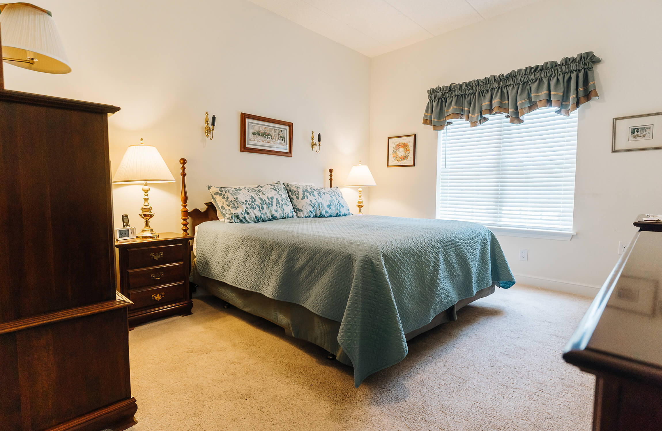 Cozy bedroom with blue bedspread and wooden furniture in a senior living unit.