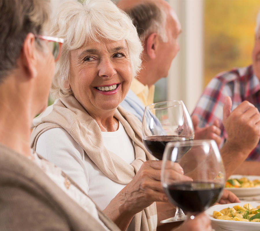 Smiling seniors enjoying wine and conversation at a dining table.