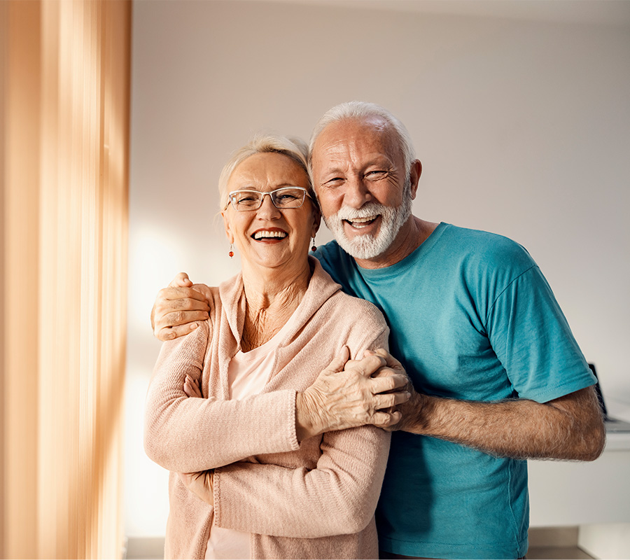 Smiling elderly couple embracing in a bright living unit of a senior community.