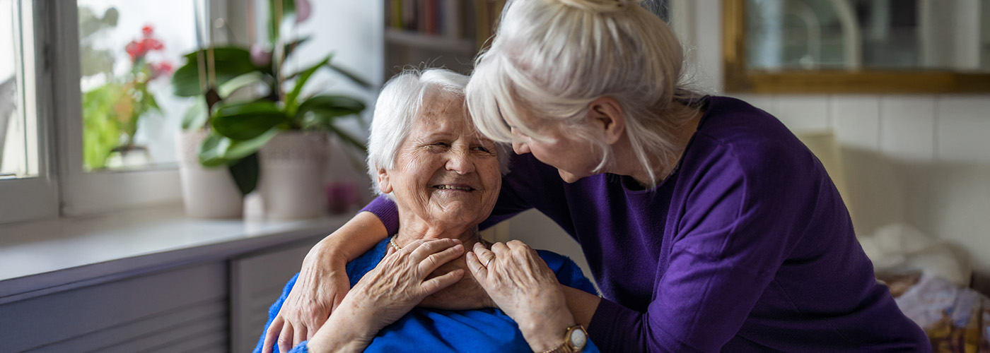 Two elderly women sharing a joyful moment in a living room, surrounded by plants.