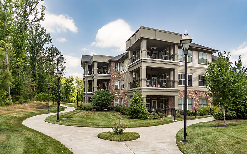 Modern Residential Building with Landscaping A modern three-story residential building with landscaped pathways and lush greenery.