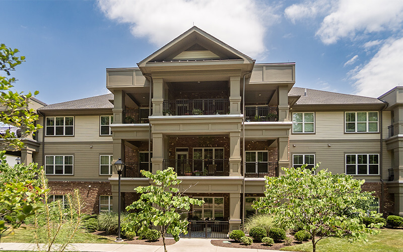 Facade of a modern senior living community building with lush greenery front.