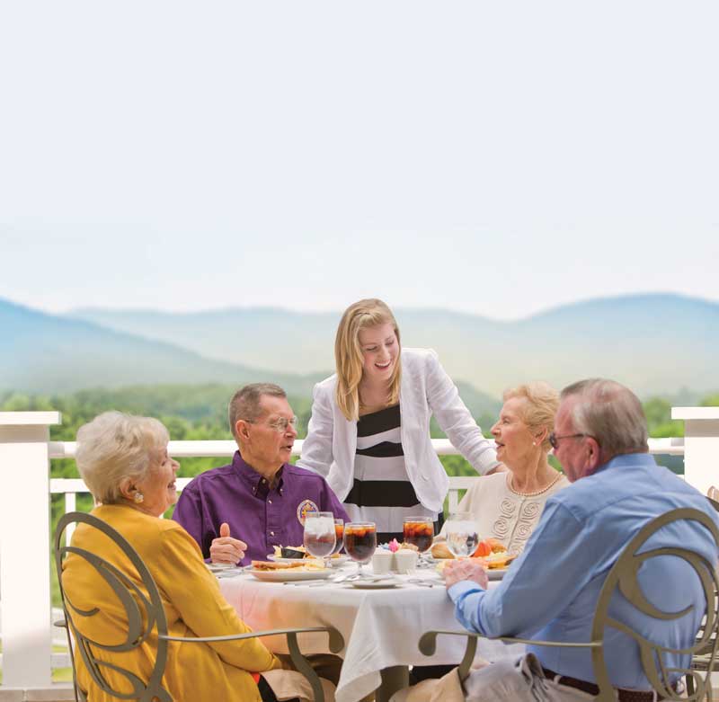Residents enjoying an outdoor meal with a caregiver at a scenic senior living community.