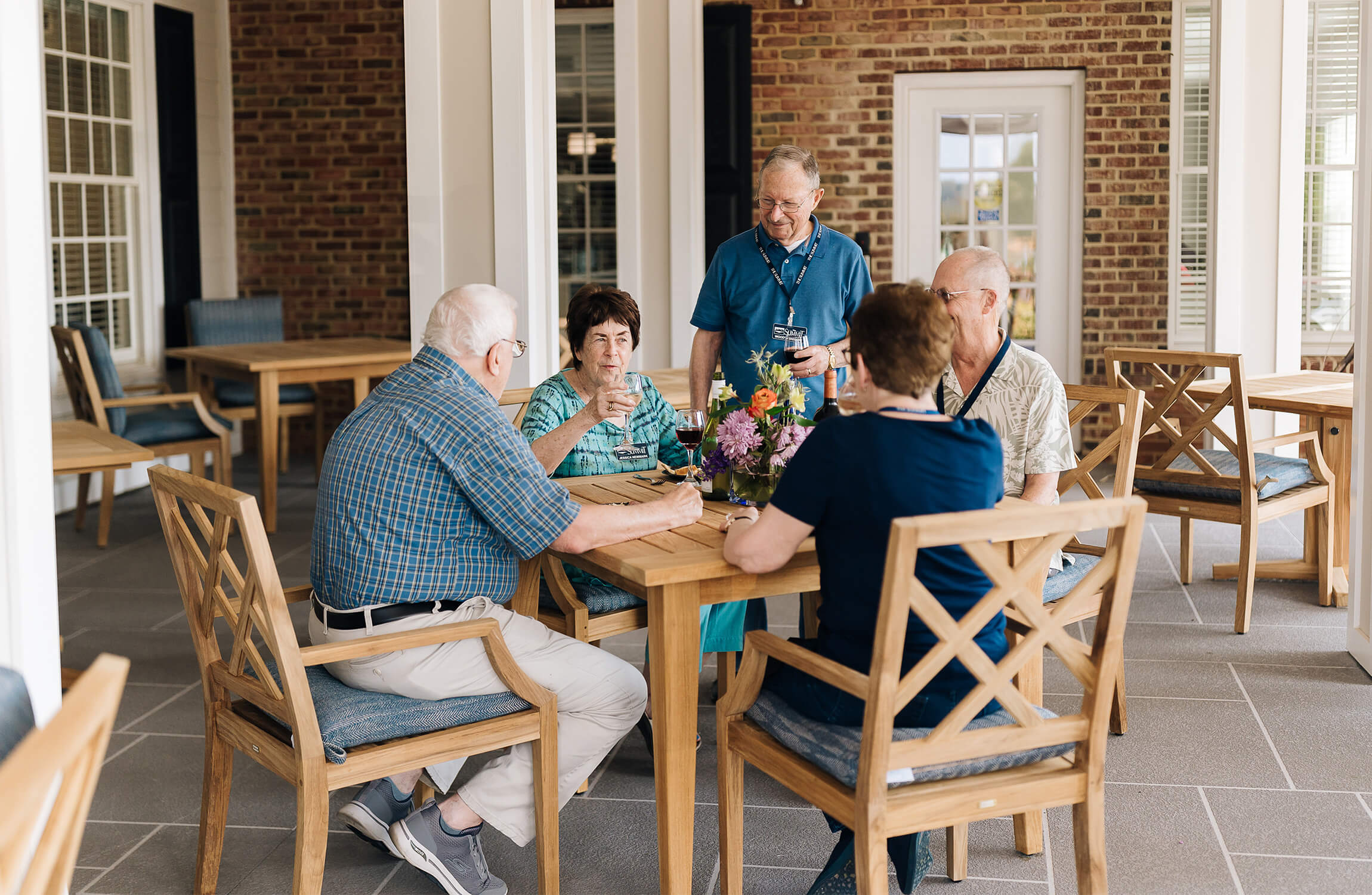 Group of seniors enjoying conversation at a wooden table outside their living units.