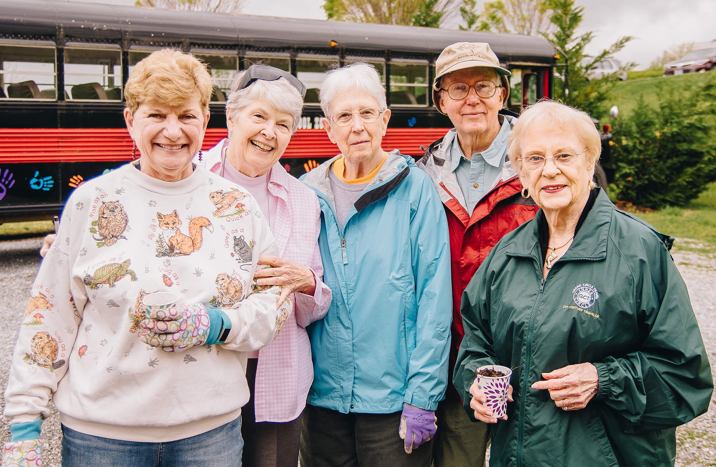 Group of seniors smiling outdoors, with a colorful bus in the background.