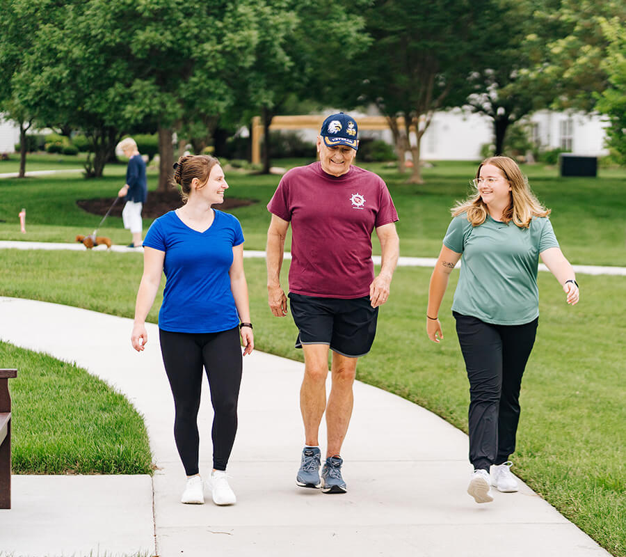 Three people walking on a pathway outdoors at a senior living community.