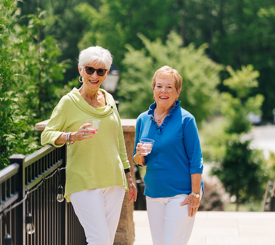 Two women enjoying drinks outside in a green garden setting.