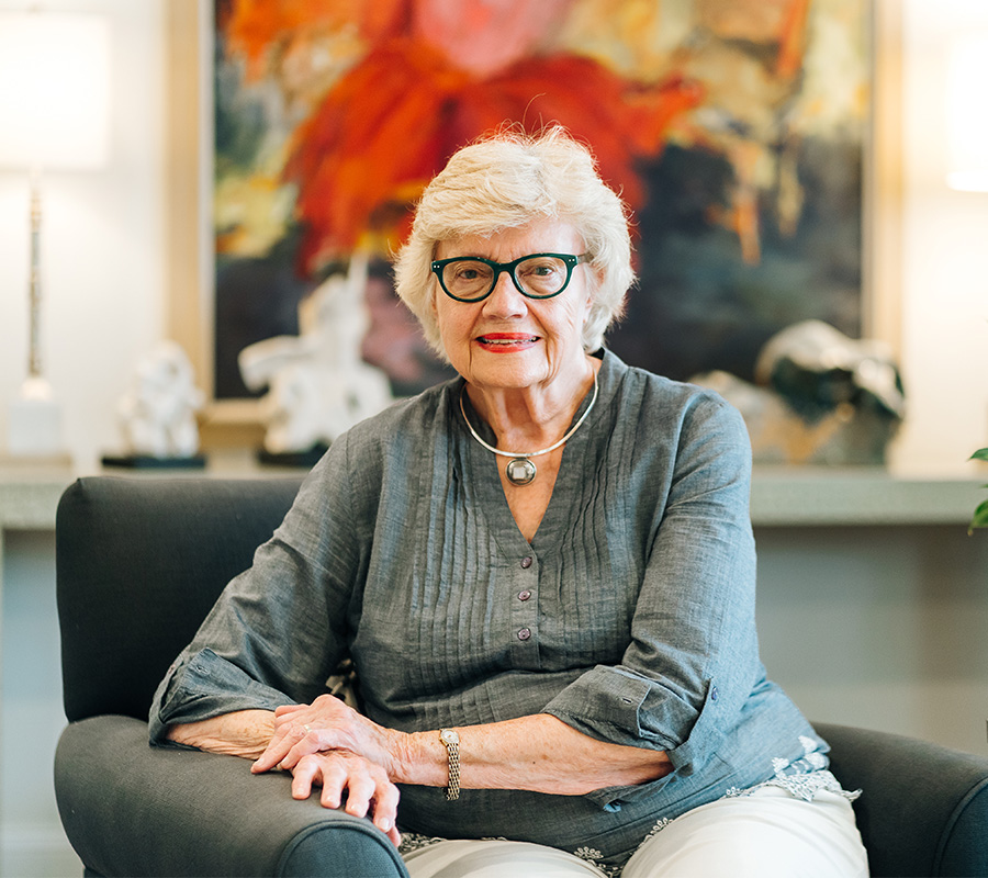 Elderly woman sitting on a chair in a warmly decorated room with abstract art.