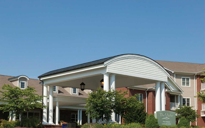 Entrance of a residential community building with covered walkway and landscaped gardens.