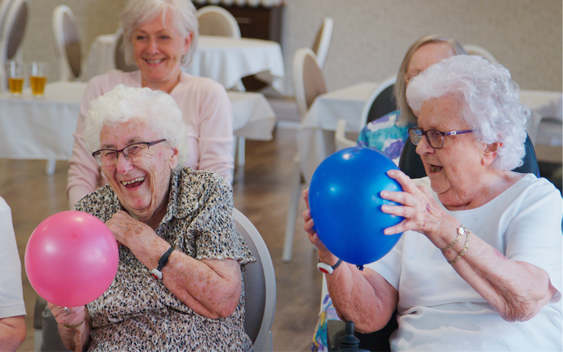 Senior residents enjoying balloon activity in a community common area.