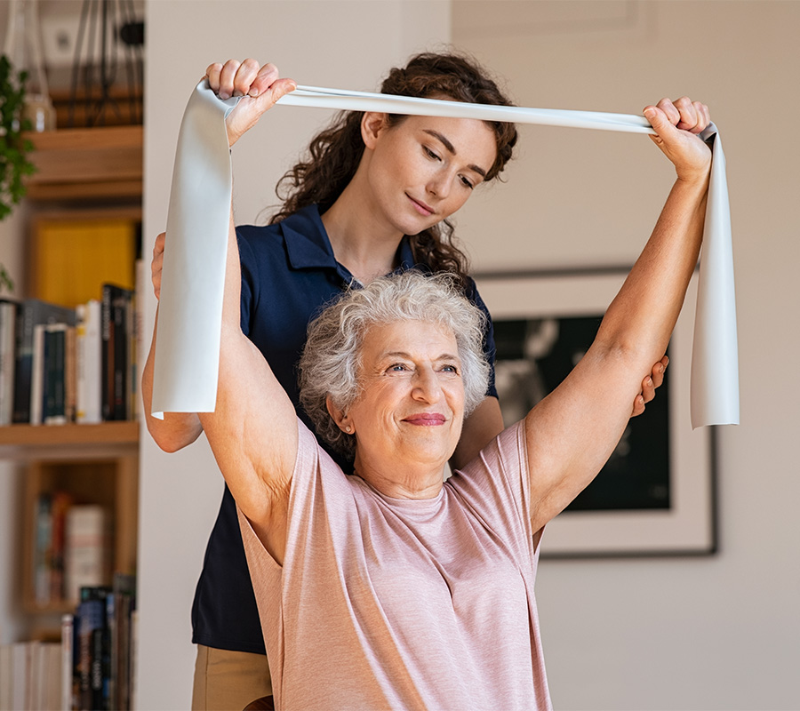 Senior woman exercising with assistance from a caregiver using a resistance band.