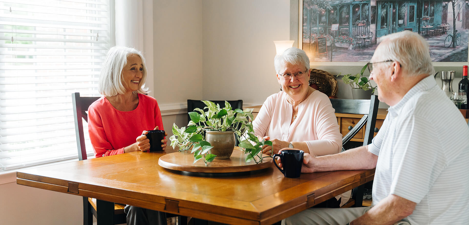 Three seniors enjoying coffee and conversation in a bright, cozy room.