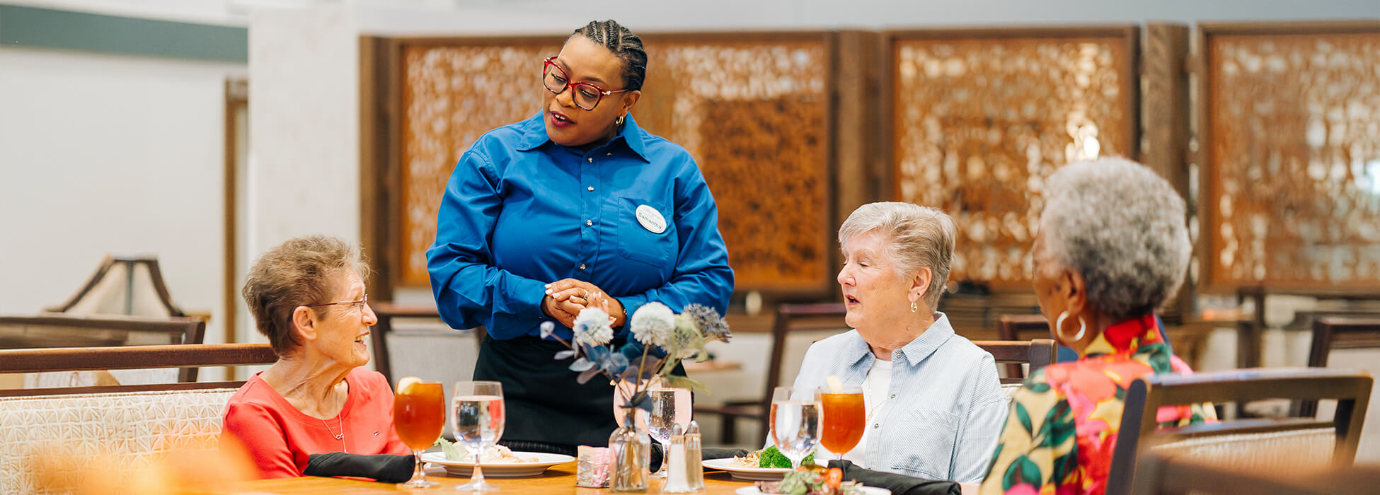 Residents dining with staff assistance in a senior community dining area.