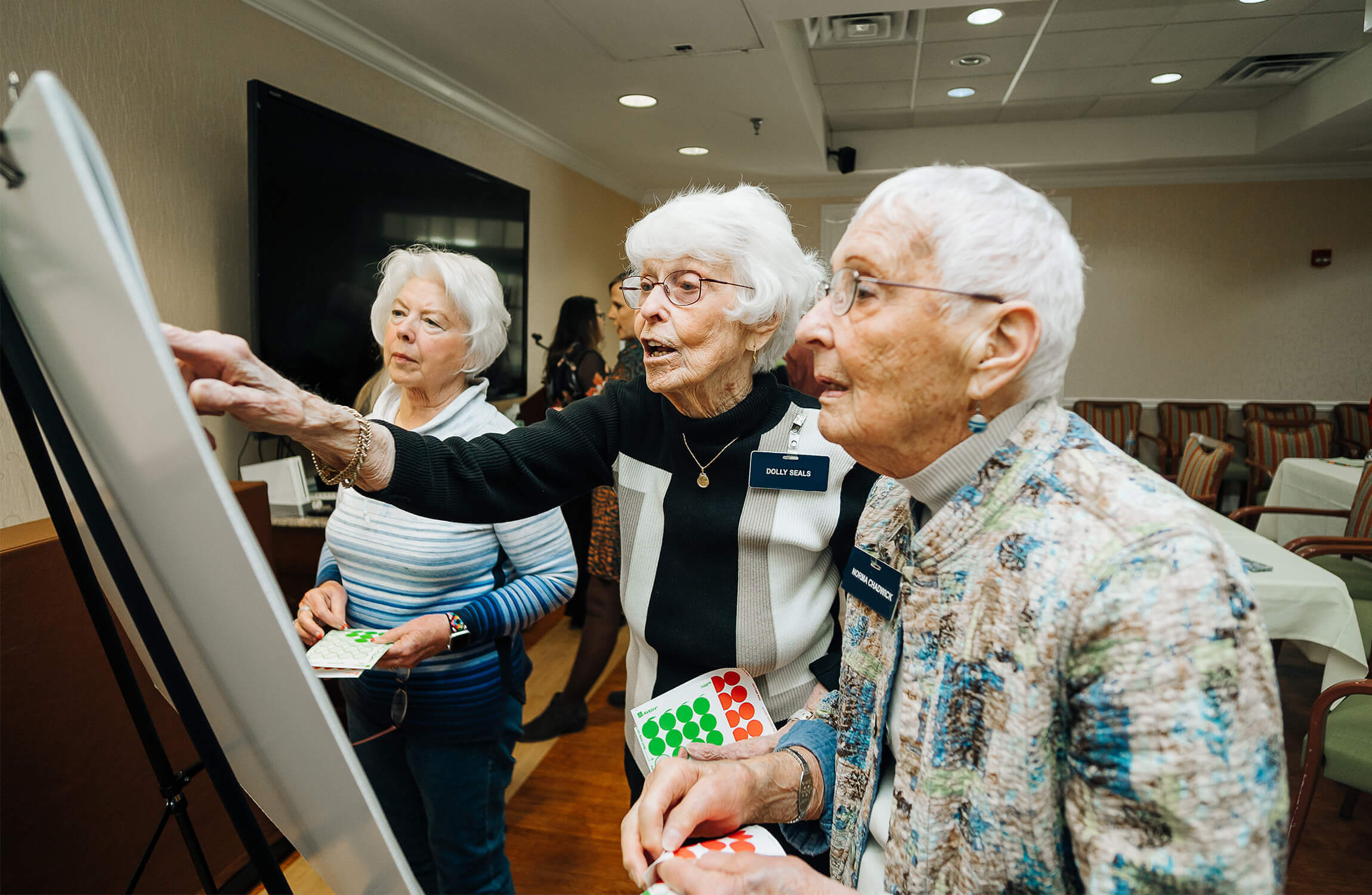Three seniors enjoying an engaging activity at their community, using colored stickers.
