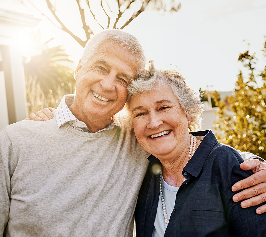 Happy senior couple embracing outside their living unit in the afternoon sun.