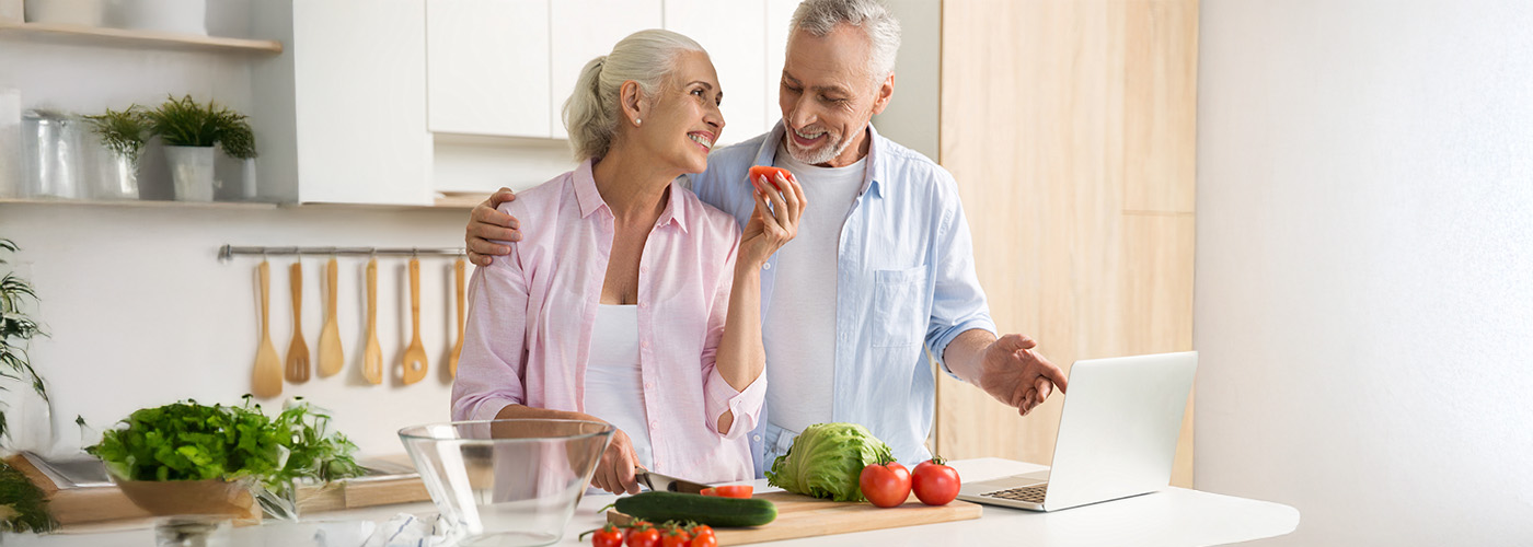 Senior couple in a modern kitchen preparing a salad with fresh vegetables.