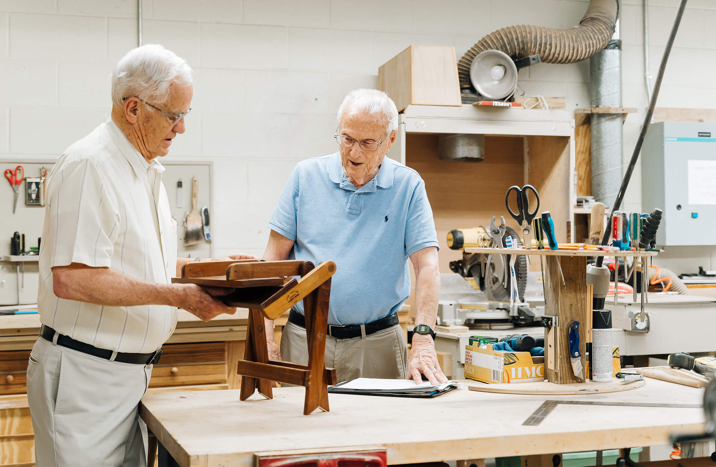 Craftsmanship in the Community Workshop Two senior men engaged in woodworking inside a well-equipped workshop.