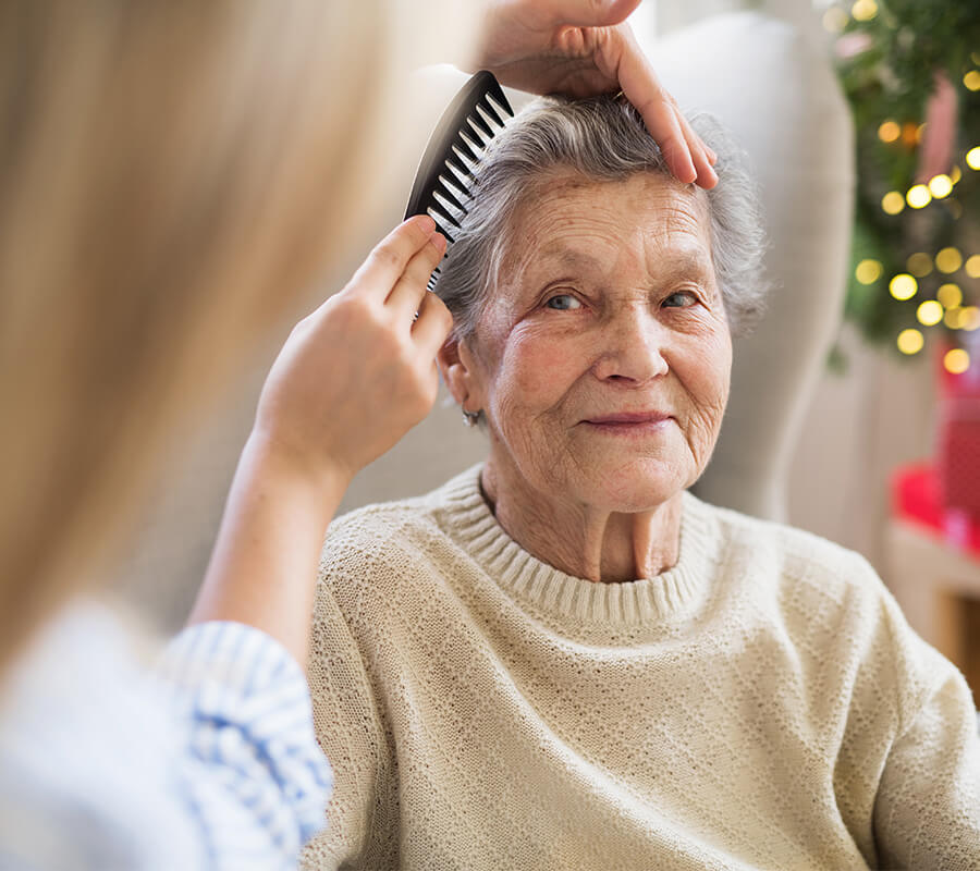 Elderly woman smiling while having her hair combed by a caregiver.