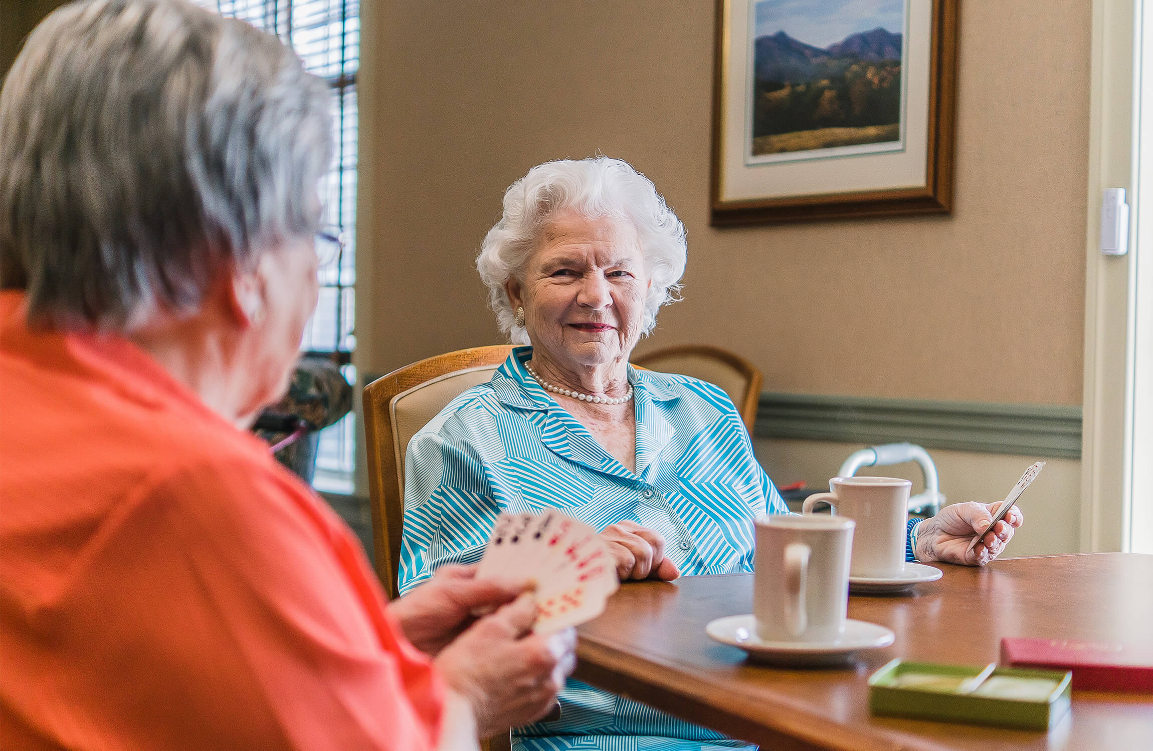 Two senior friends in a cozy lounge playing cards and enjoying coffee together.