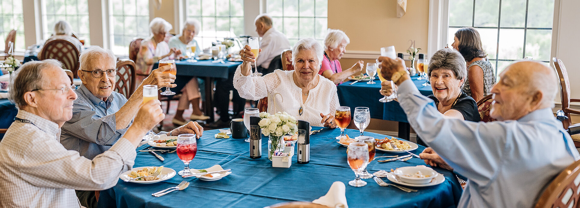 Group of elderly individuals raising glasses in a dining area of a senior living community.