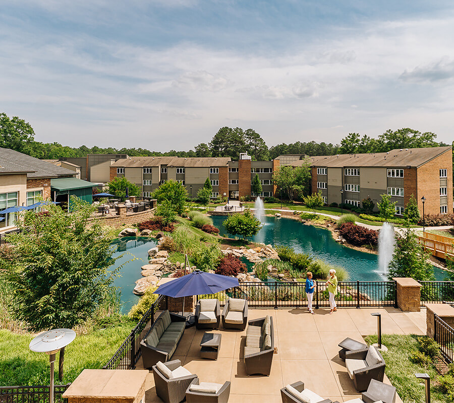 Scenic view of a senior living community with a pond and fountains.