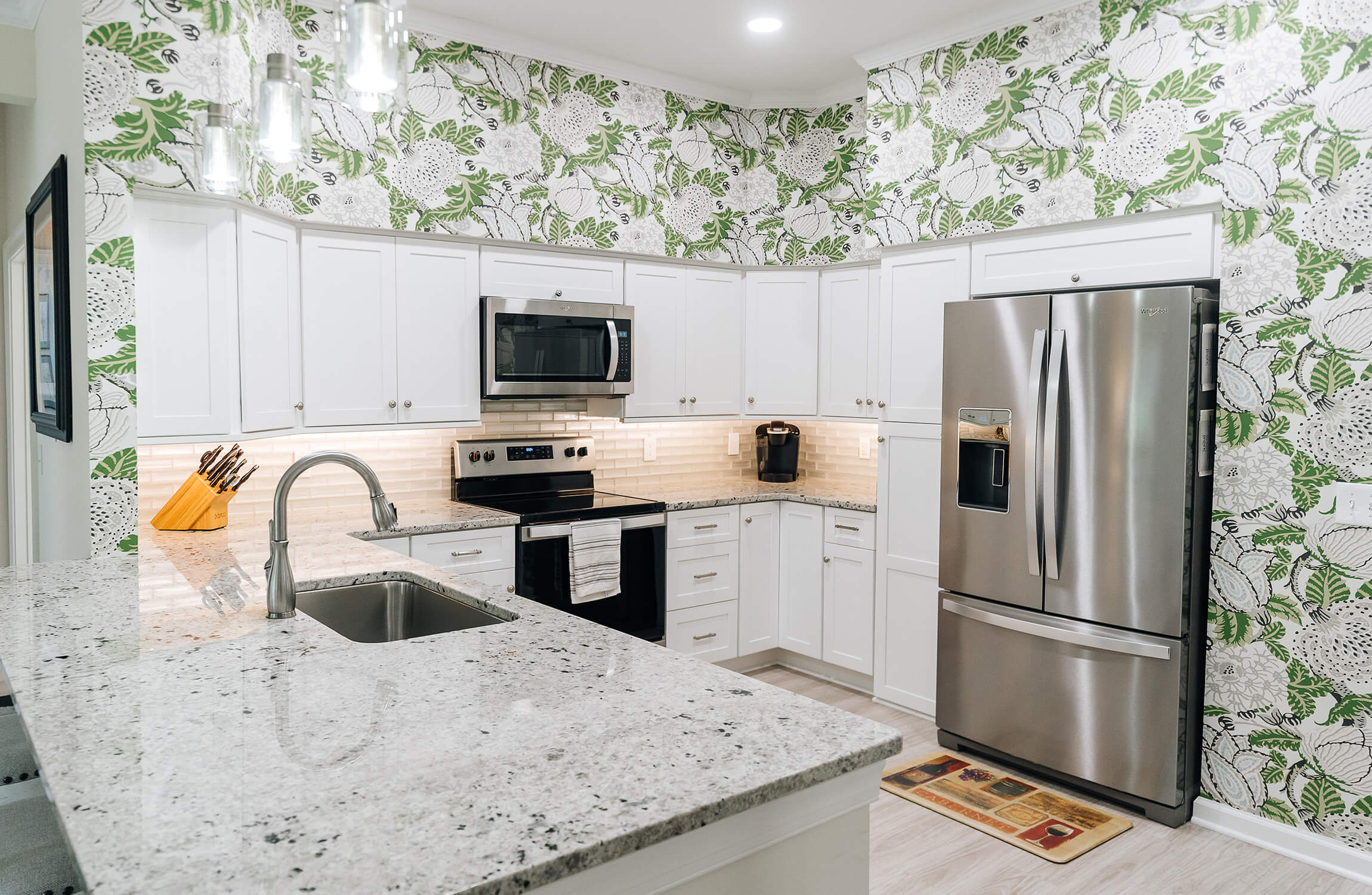 Modern kitchen in a senior living unit with floral wallpaper and stainless steel appliances.