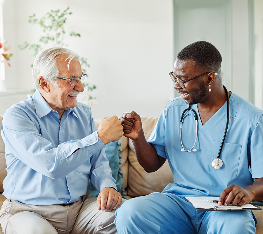 Senior man and nurse fist bump on couch