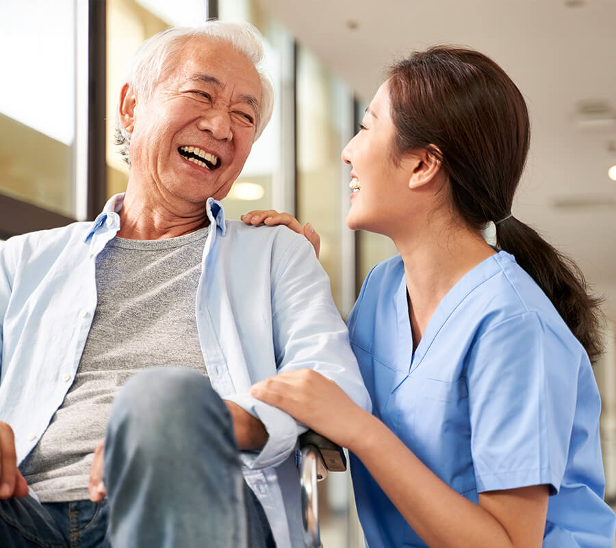 Senior man in wheel chair smiles with caregiver nurse