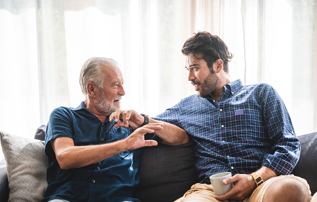 Adult son and elderly father talk on the couch