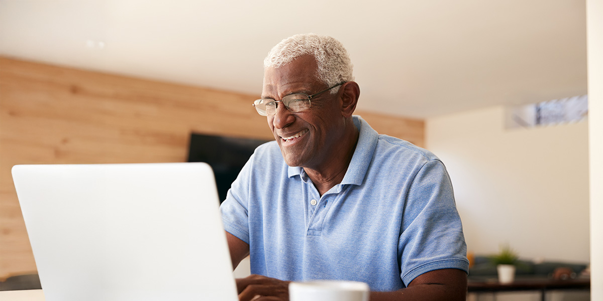 Senior man smiles at laptop in his living room