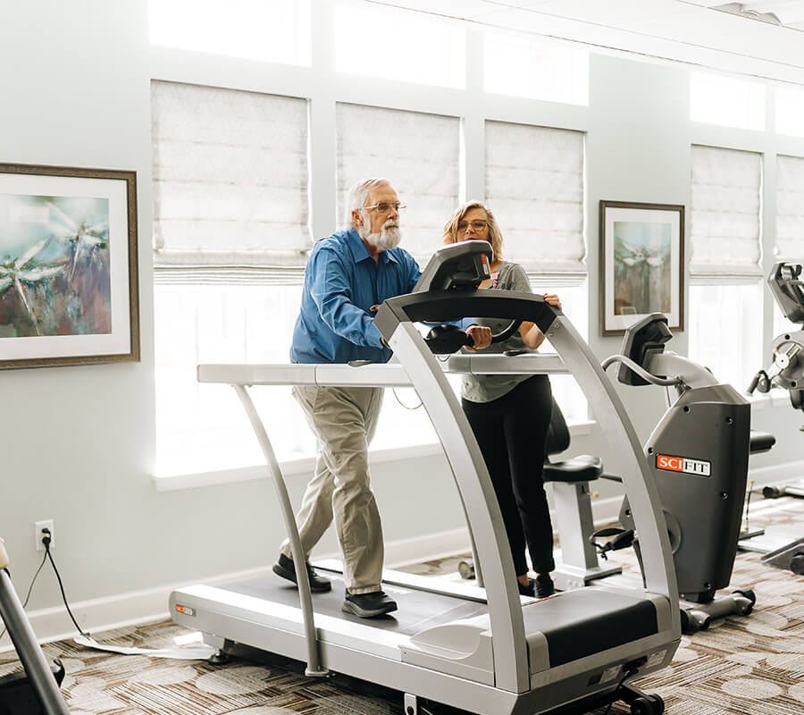 Senior man walks on treadmill with therapist