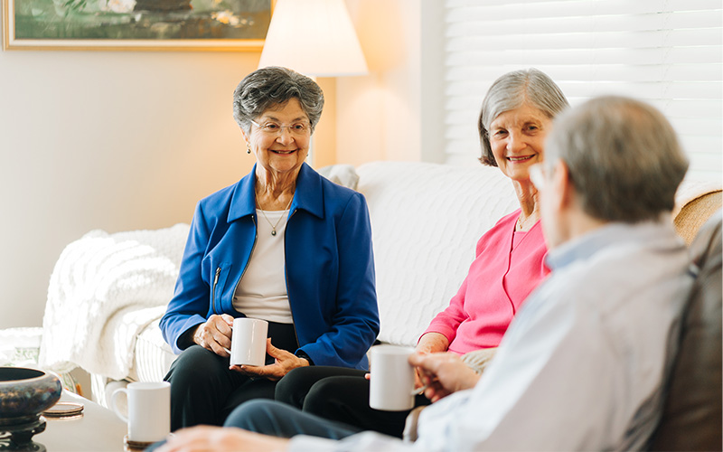 Three seniors enjoying coffee and conversation in a cozy living unit.