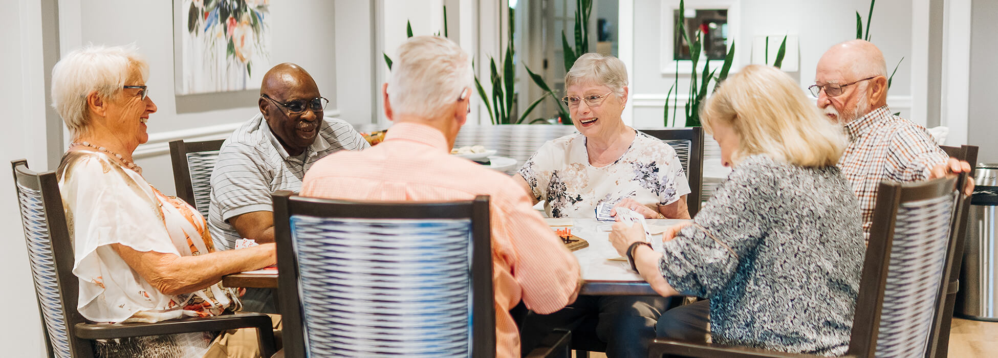 Group of seniors seated around a table in a communal living area.