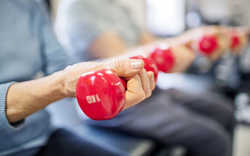 Seniors exercising with red dumbbells in a community gym.