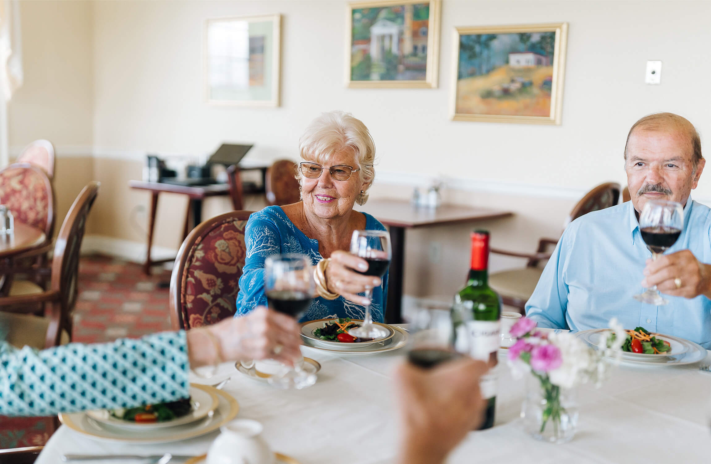 Group of seniors in a dining area toasting with glasses of red wine.