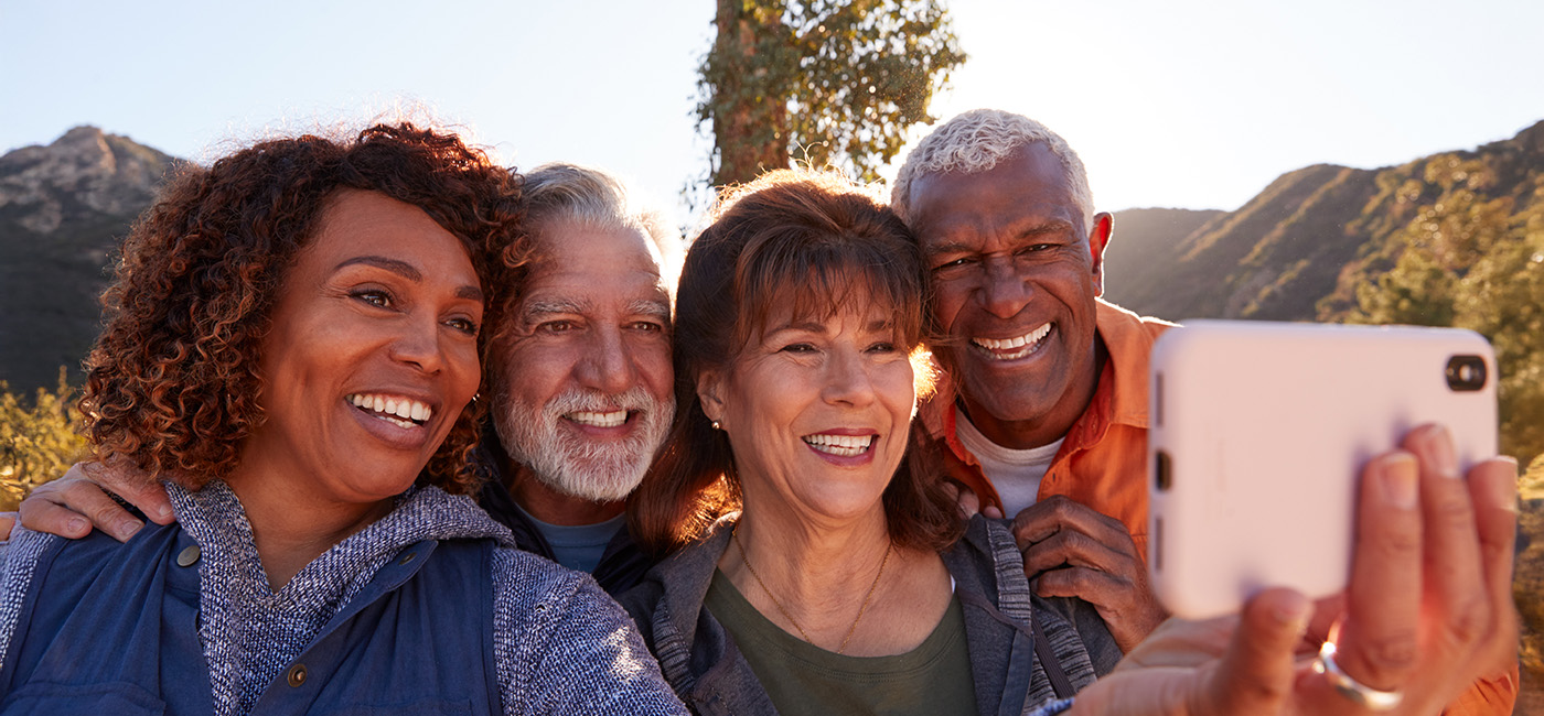 Four seniors taking a selfie outdoors, smiling with mountains in the background.