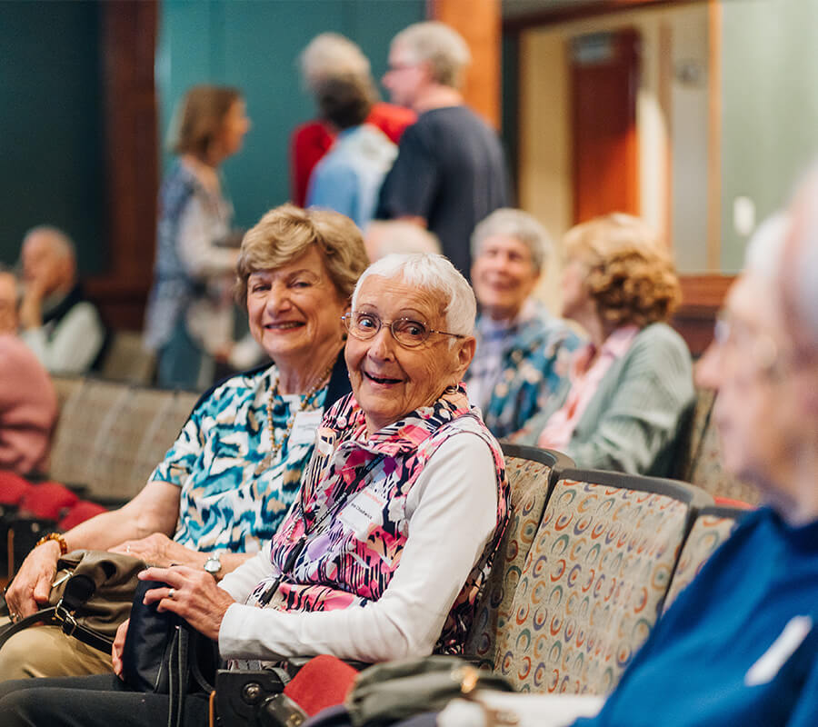 Two senior women smile in an auditorium