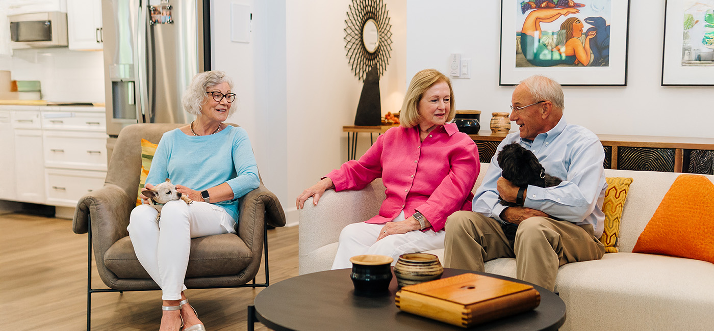 Three seniors talking with small dogs in a cozy living area with modern decor.