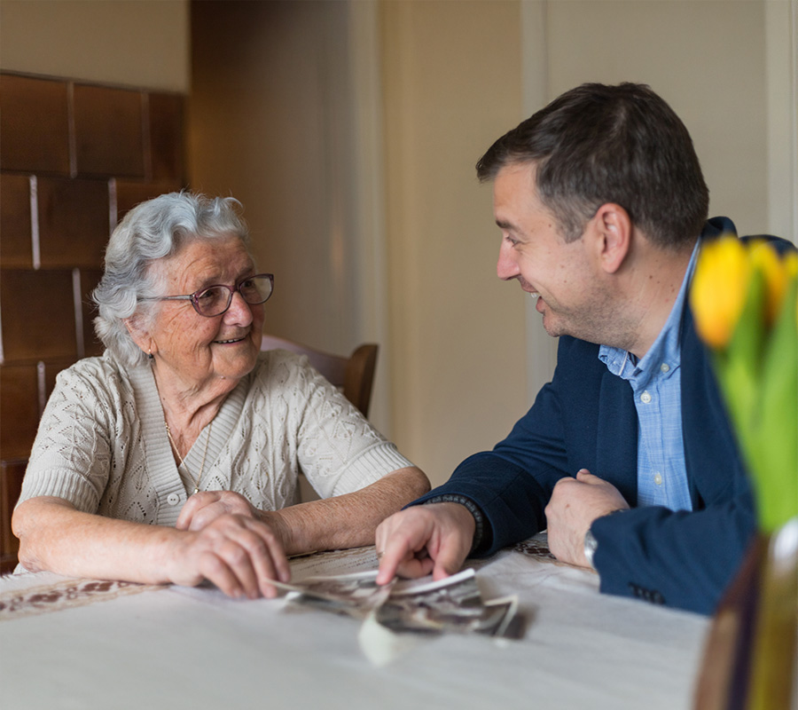 Elderly woman and man sitting at a table, smiling and looking at photographs.