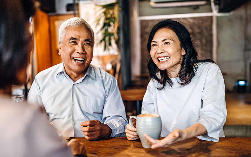 Smiling senior couple enjoying coffee at a wooden table indoors.